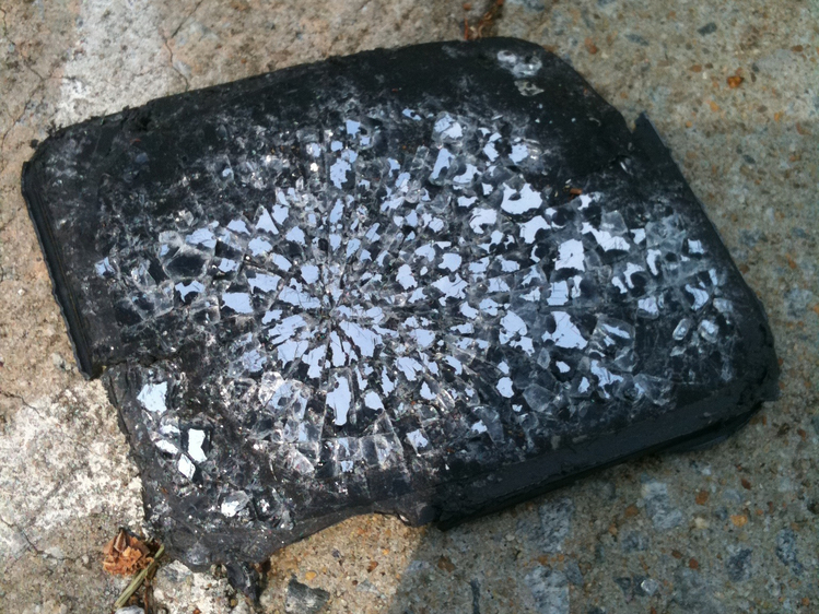 A side view mirror from a car, shattered and bent lying on the pavement.